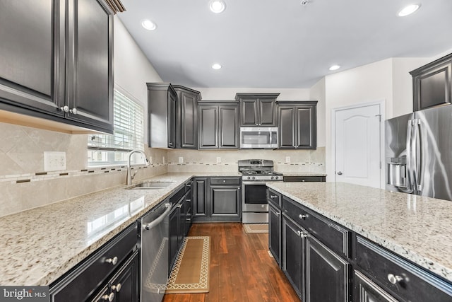 kitchen featuring dark wood-style floors, a sink, dark cabinetry, light stone countertops, and appliances with stainless steel finishes