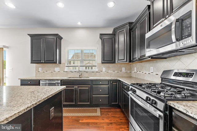 kitchen with recessed lighting, dark wood finished floors, dark cabinets, a sink, and appliances with stainless steel finishes