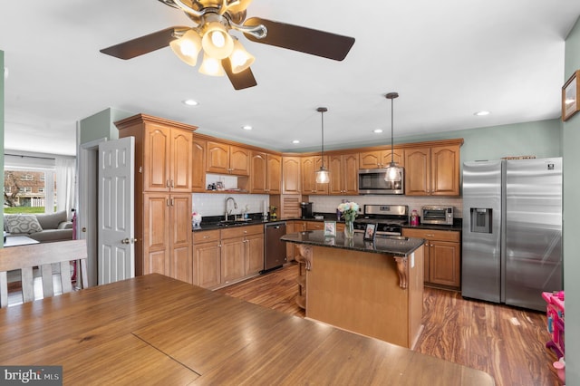 kitchen with a sink, decorative backsplash, light wood-type flooring, a breakfast bar, and appliances with stainless steel finishes