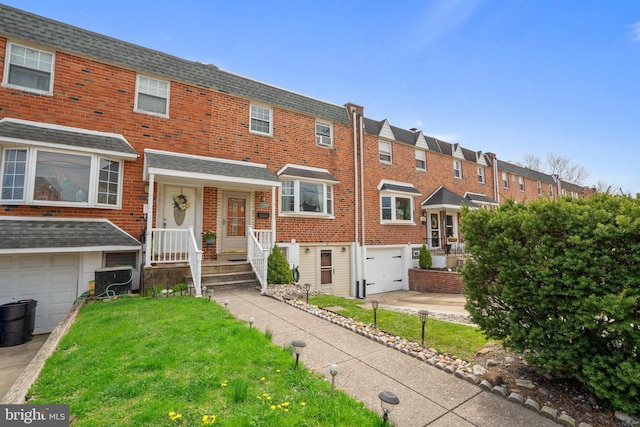 townhome / multi-family property with a front lawn, an attached garage, a shingled roof, and brick siding