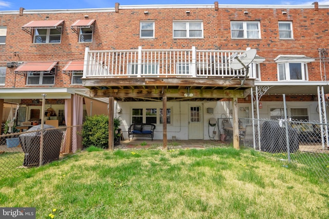 rear view of property featuring fence, a wooden deck, a lawn, and brick siding