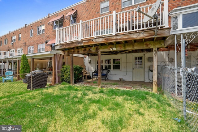 rear view of house with a deck, brick siding, fence, and a lawn