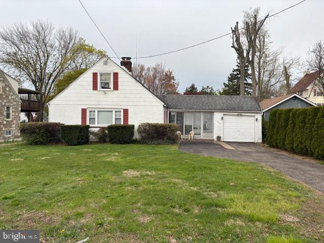 view of front of house with a chimney, aphalt driveway, a garage, and a front yard