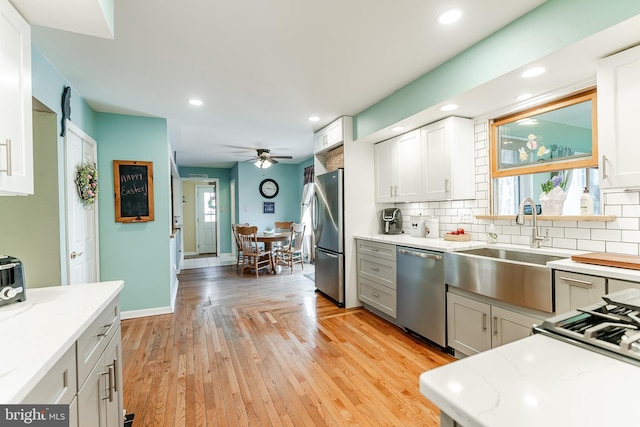 kitchen with a sink, decorative backsplash, ceiling fan, stainless steel appliances, and light wood finished floors