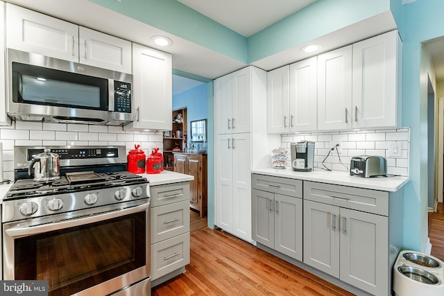 kitchen with light wood-style flooring, backsplash, gray cabinetry, light countertops, and appliances with stainless steel finishes