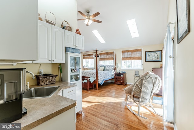 bedroom featuring high vaulted ceiling, a sink, light wood finished floors, and a skylight