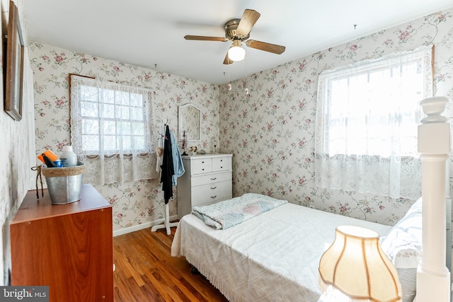 bedroom with wallpapered walls, wood finished floors, baseboards, and multiple windows