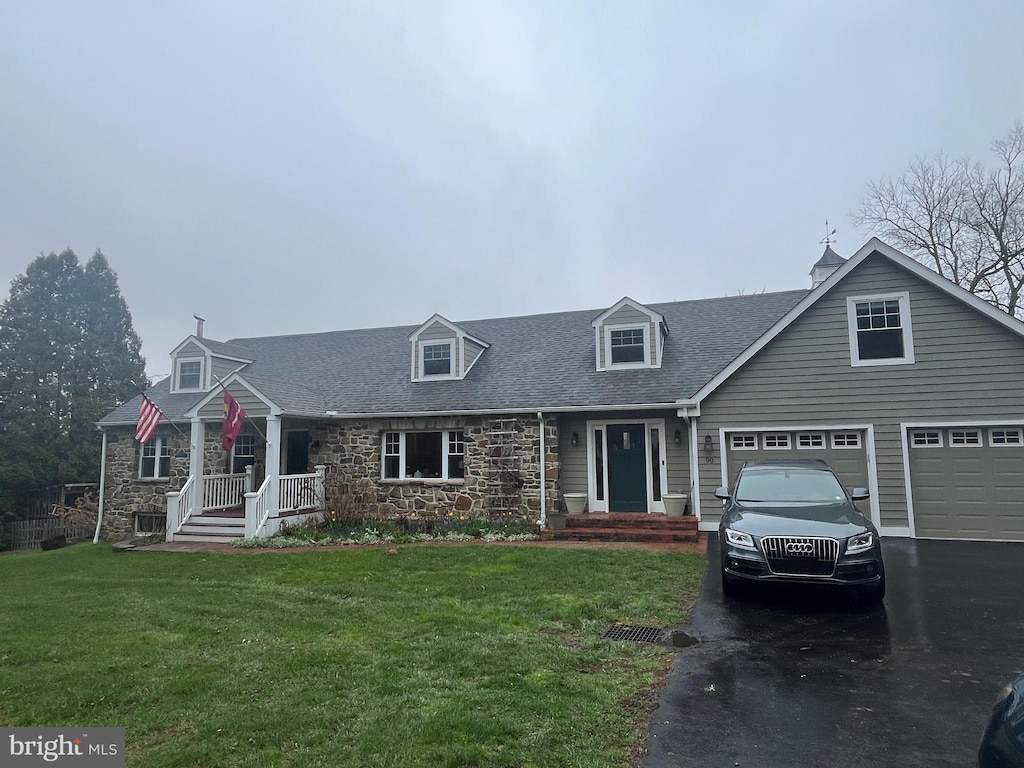 cape cod-style house with stone siding, driveway, a front lawn, and a shingled roof
