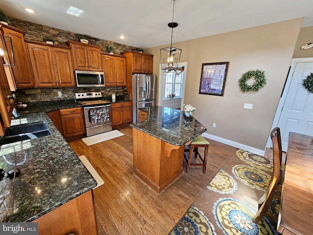 kitchen with an inviting chandelier, backsplash, wood finished floors, brown cabinetry, and appliances with stainless steel finishes