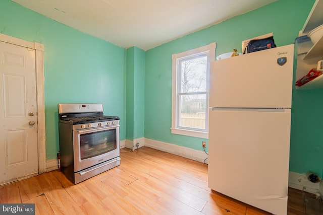 kitchen with baseboards, light wood-style flooring, stainless steel gas range oven, and freestanding refrigerator