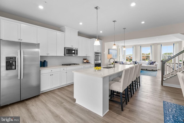 kitchen with a sink, an island with sink, light wood-style floors, stainless steel appliances, and white cabinets
