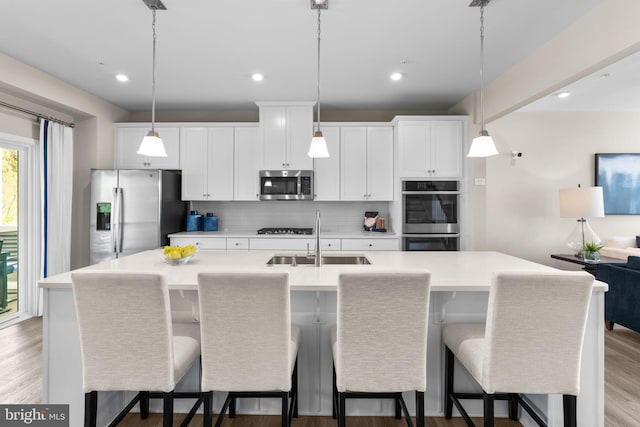 kitchen featuring stainless steel appliances, light countertops, a sink, light wood-type flooring, and tasteful backsplash