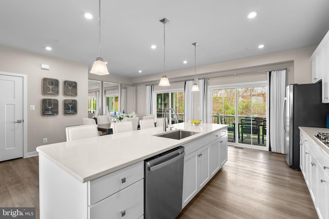 kitchen featuring an island with sink, stainless steel appliances, light countertops, a sink, and white cabinetry