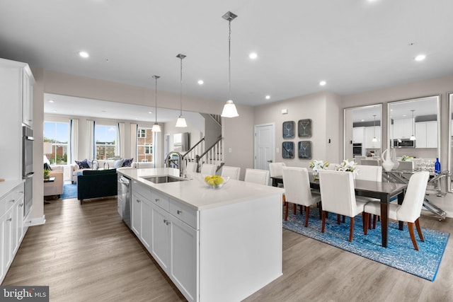 kitchen featuring light wood-style flooring, a sink, a center island with sink, open floor plan, and appliances with stainless steel finishes