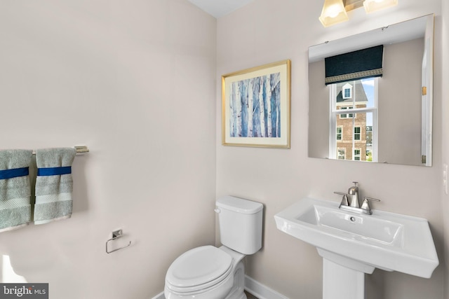 half bath with toilet, a sink, and baseboards