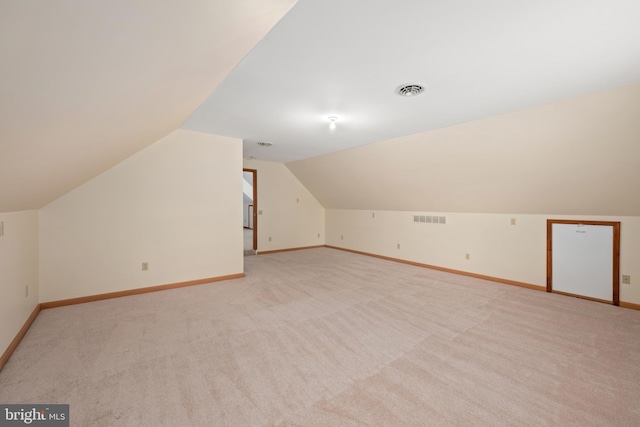 additional living space with baseboards, vaulted ceiling, visible vents, and light colored carpet