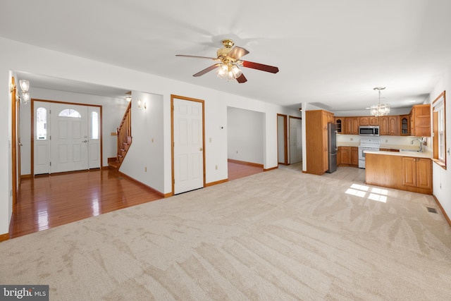 unfurnished living room with stairway, a sink, ceiling fan with notable chandelier, light carpet, and visible vents