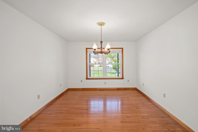 spare room with baseboards, a notable chandelier, and light wood-style flooring