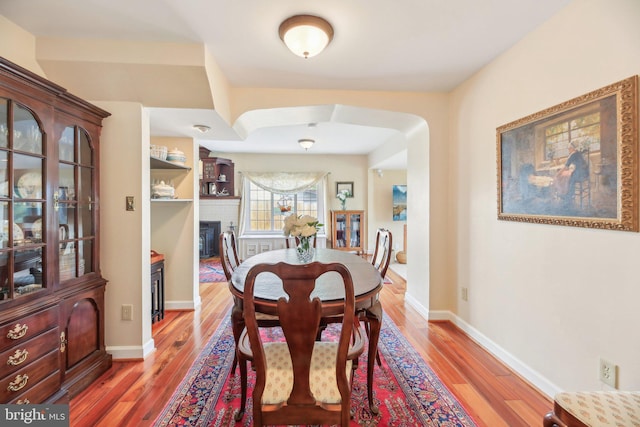 dining room with baseboards, a brick fireplace, wood finished floors, and arched walkways