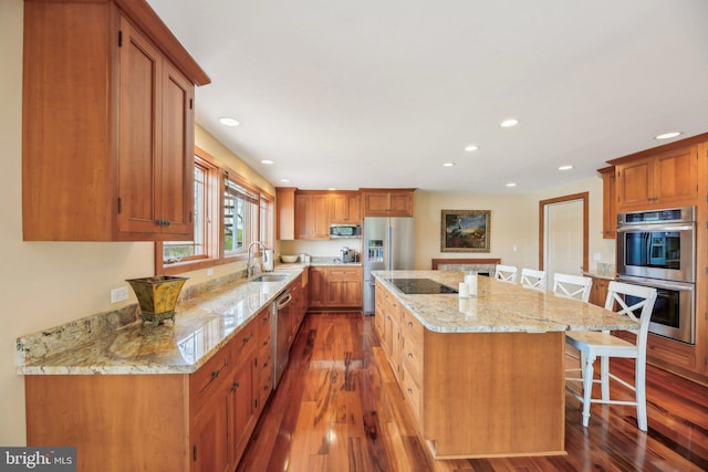kitchen featuring a sink, a kitchen bar, wood finished floors, a kitchen island, and appliances with stainless steel finishes
