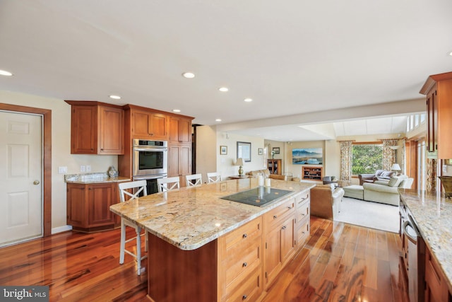 kitchen with black electric cooktop, wood finished floors, a kitchen island, and double oven