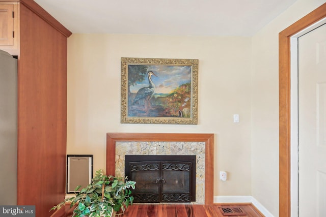 living area featuring a premium fireplace, wood finished floors, visible vents, and baseboards