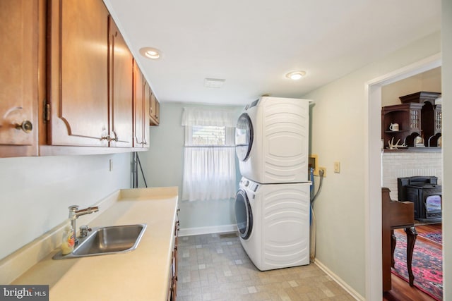 washroom with stacked washer and dryer, a sink, baseboards, cabinet space, and a wood stove