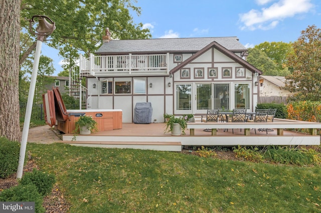 rear view of house with a hot tub, a yard, stucco siding, a wooden deck, and roof with shingles