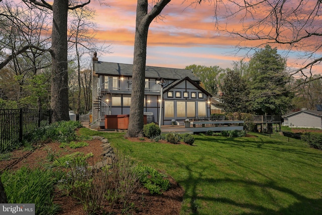 rear view of property featuring a chimney, a fenced backyard, a balcony, a lawn, and a hot tub