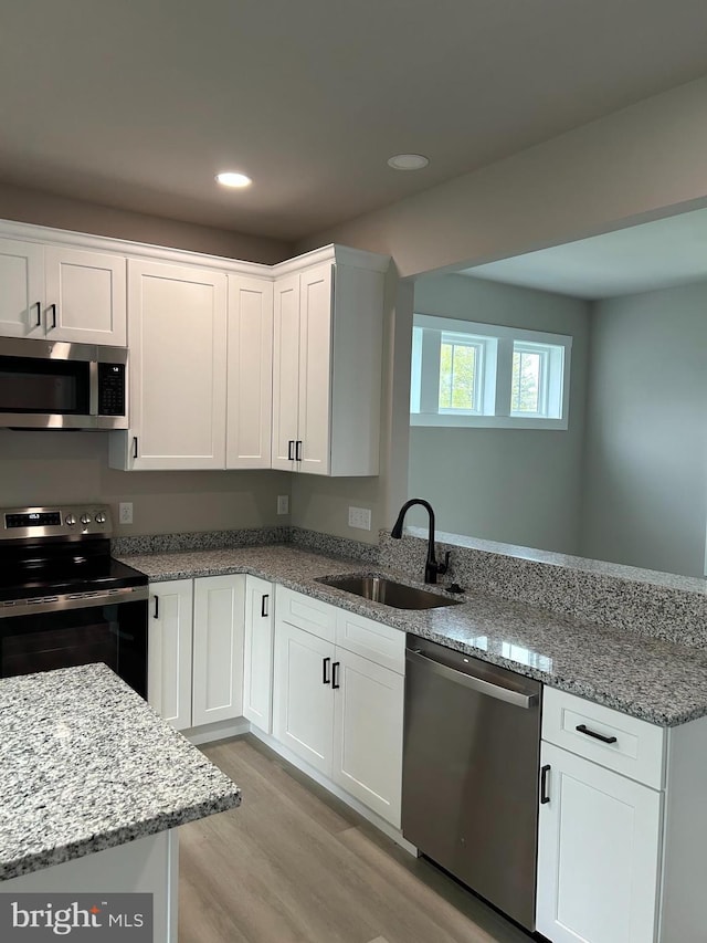kitchen with a sink, light wood-style floors, a peninsula, white cabinetry, and stainless steel appliances