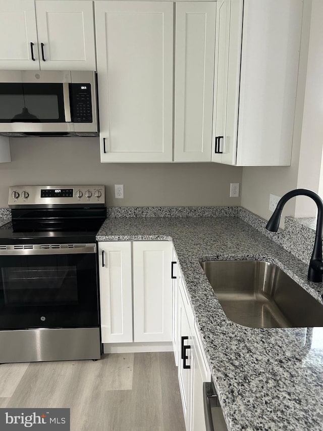 kitchen featuring light wood-type flooring, light stone counters, white cabinetry, appliances with stainless steel finishes, and a sink
