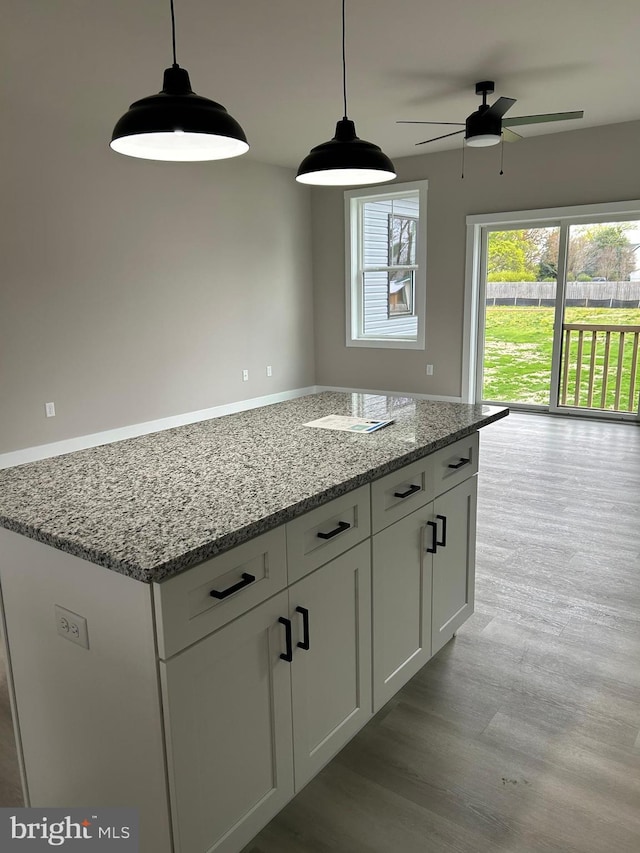 kitchen with ceiling fan, light stone countertops, white cabinets, a kitchen island, and hanging light fixtures