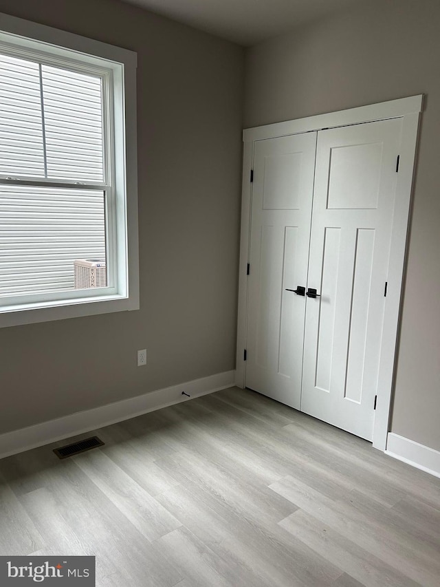 unfurnished bedroom featuring light wood-style flooring, baseboards, multiple windows, and visible vents