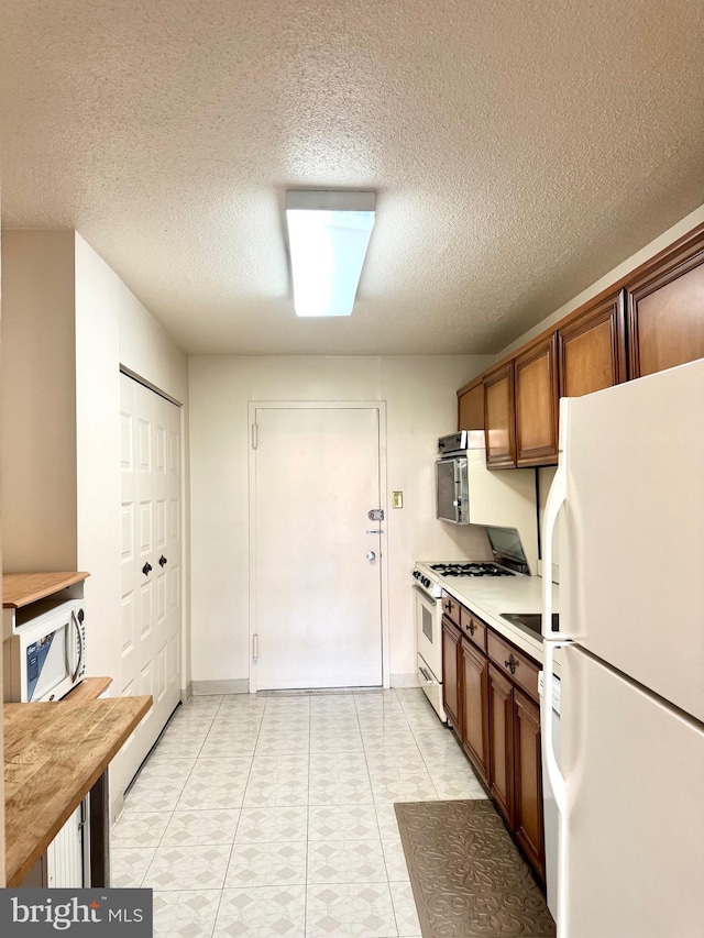 kitchen featuring white appliances, a textured ceiling, light tile patterned floors, and light countertops