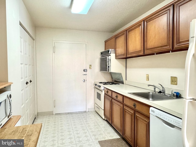 kitchen featuring white appliances, light countertops, a textured ceiling, brown cabinets, and a sink