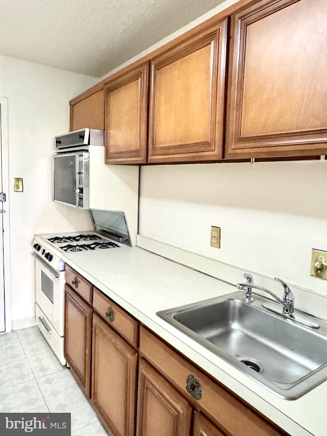 kitchen with brown cabinets, a sink, light countertops, a textured ceiling, and white range with gas cooktop