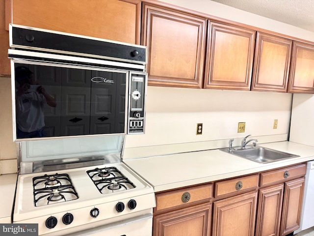 kitchen with light countertops, oven, white range with gas cooktop, and a sink