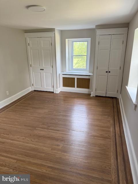 639 Old Airport Rd, Douglassville, PA 19518 - unfurnished bedroom featuring radiator heating unit, dark wood finished floors, baseboards, and multiple closets