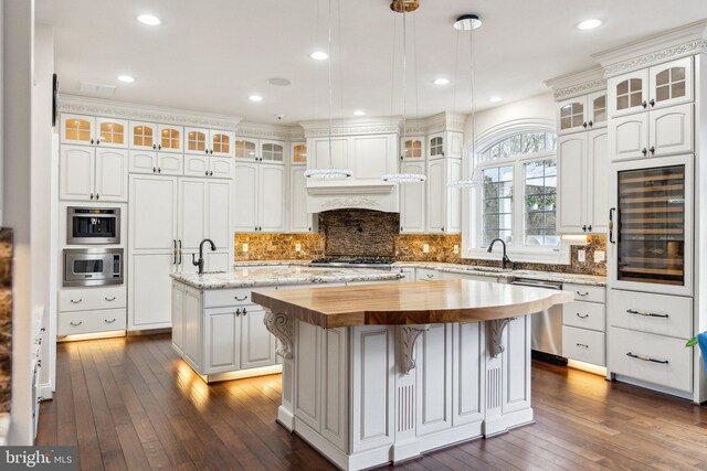 kitchen featuring a kitchen island with sink, wooden counters, beverage cooler, dark wood finished floors, and appliances with stainless steel finishes