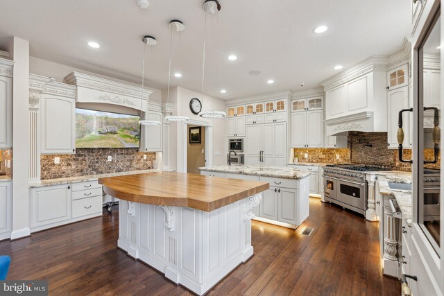 kitchen featuring an island with sink, butcher block counters, backsplash, and range with two ovens