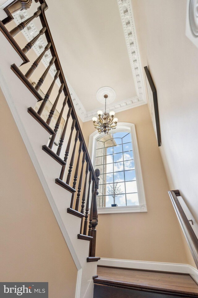 stairs with baseboards, ornamental molding, wood finished floors, and a chandelier