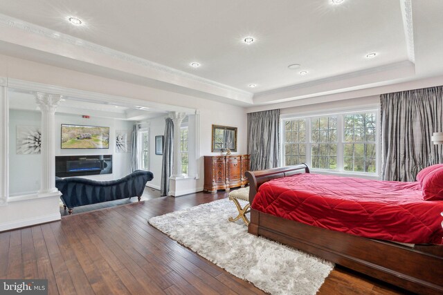 bedroom featuring a raised ceiling, a fireplace, decorative columns, and hardwood / wood-style flooring