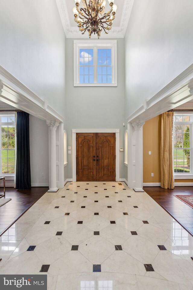 tiled foyer entrance with crown molding, a high ceiling, ornate columns, and a notable chandelier