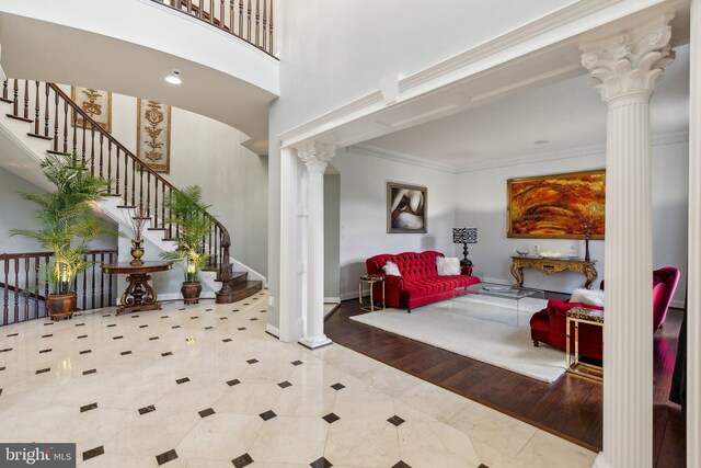 tiled foyer entrance featuring decorative columns, a towering ceiling, crown molding, baseboards, and stairs