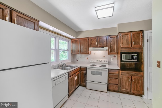 kitchen with a sink, white appliances, light countertops, backsplash, and under cabinet range hood