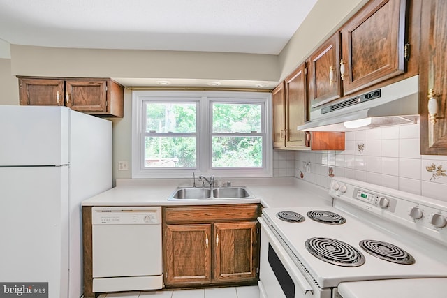 kitchen with white appliances, light countertops, under cabinet range hood, tasteful backsplash, and a sink