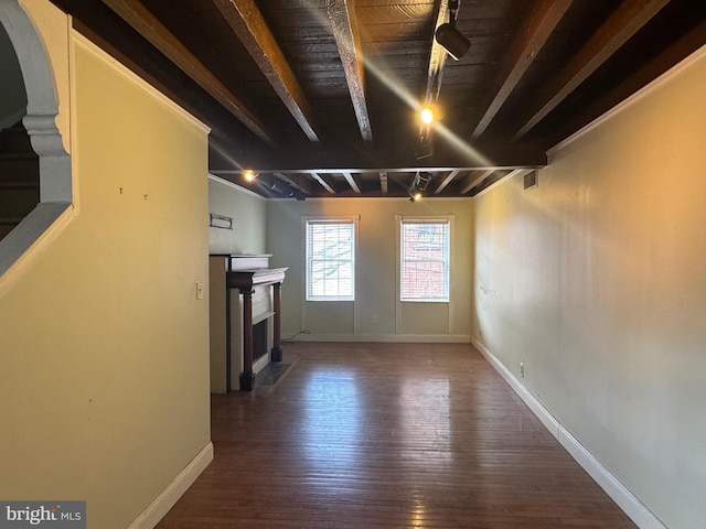 unfurnished living room featuring wood-type flooring, beamed ceiling, baseboards, arched walkways, and a fireplace with flush hearth