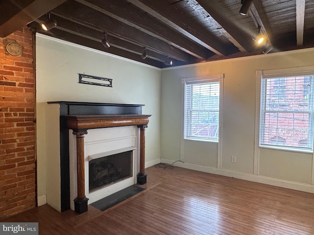 unfurnished living room featuring a fireplace with flush hearth, track lighting, beam ceiling, and hardwood / wood-style flooring
