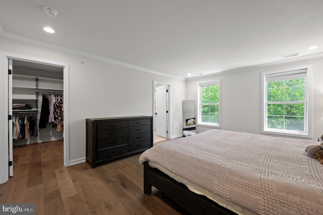 bedroom featuring wood finished floors, a walk in closet, visible vents, ornamental molding, and recessed lighting