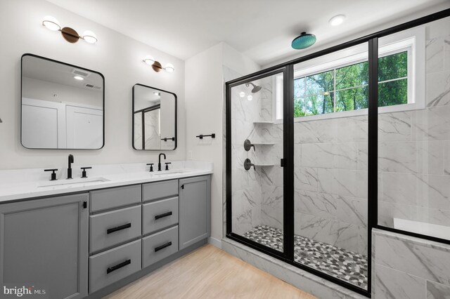 full bathroom with a marble finish shower, double vanity, and a sink